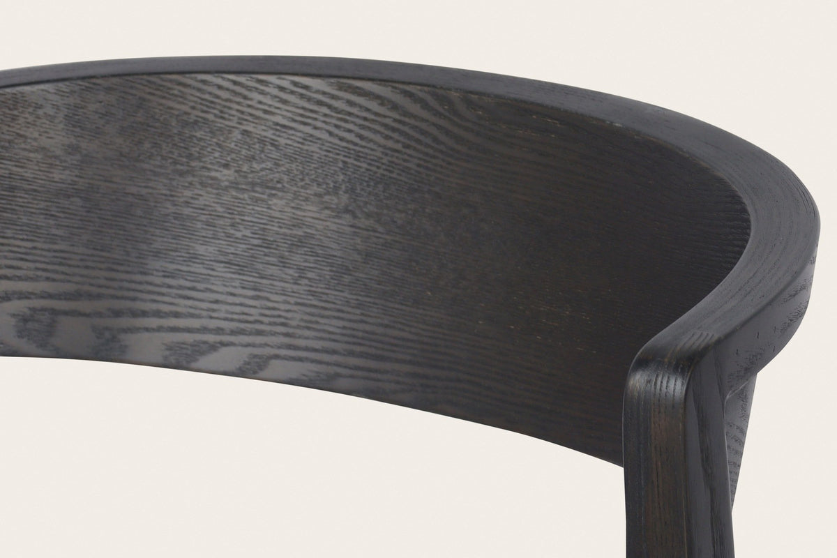 Close-up of a Certosa chair in mocha: the curved back band of ash veneer rolling round the top of the rear leg
