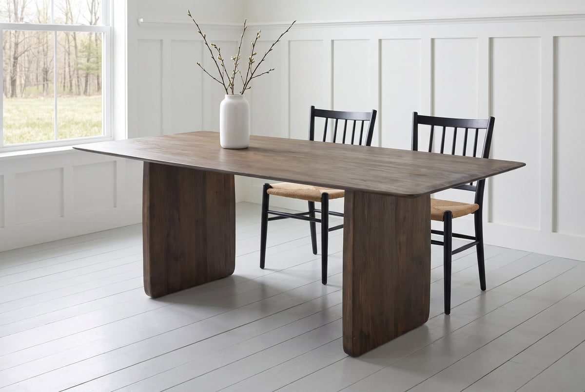Arquata dining table in mocha mango wood in a white board-and-batten dining room in Knowlton with black spindle chairs, a meadow and woods through the window