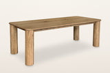 Atzara oak dining table in Natural, three-quarter view on a warm white studio backdrop: a long top with rounded corners on fo