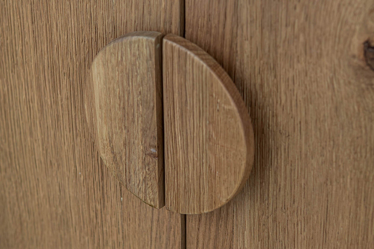 Close-up of the Atzara Small round pull in Natural, split in half where the two oak doors meet