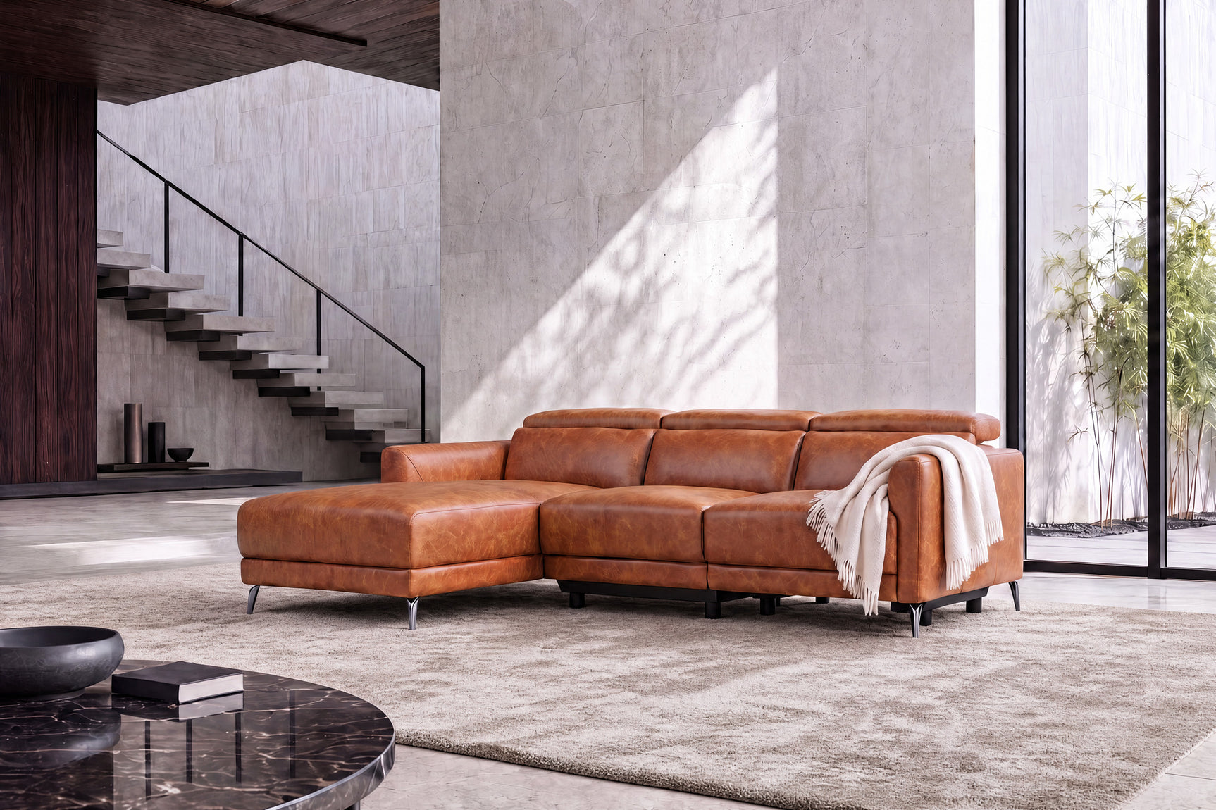 Wide view of the Andria cognac leather sectional with chaise and draped throw in a modern room
