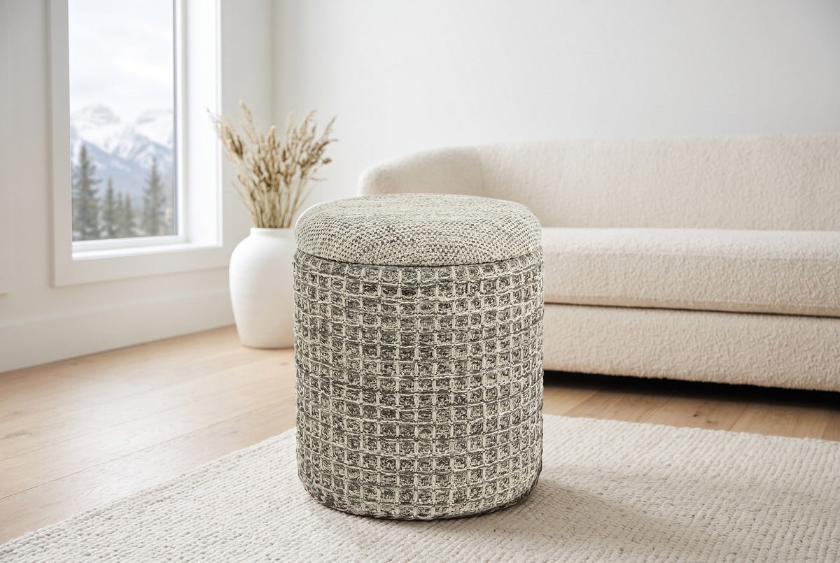 A Balme pouf in Charcoal on a cream wool rug in a mountain house living room in Canmore, a cream boucle sofa behind and snowy peaks through the window