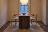 Bardolino round table in a limewashed townhouse dining room at dusk, a paper pendant above and two chairs pulled back