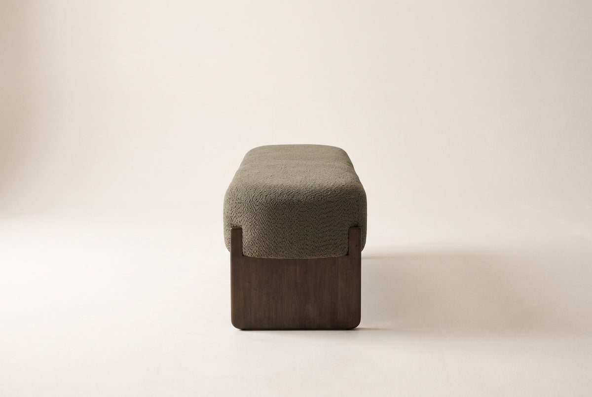 The dark green Bassano bench seen from the end: the rounded boucle seat on one dark rubberwood slab leg