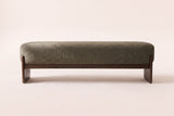 The Bassano bench in dark green loop-yarn boucle on dark rubberwood slab legs, straight front view on an off-white studio background