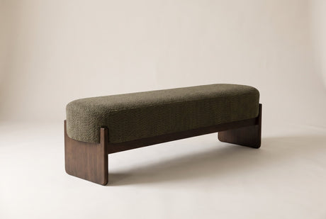 The Bassano bench in dark green loop-yarn boucle on dark rubberwood slab legs, front three-quarter view on an off-white studio background