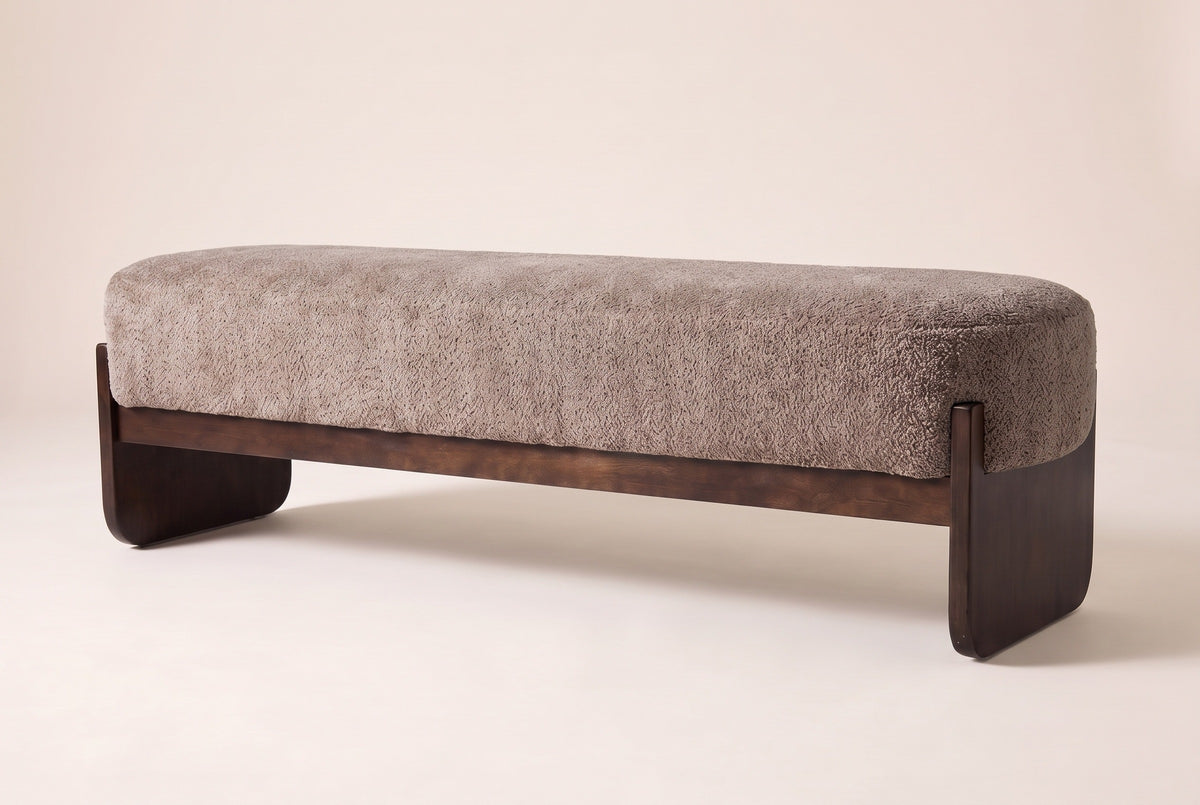 Bassano bench in light brown loop-yarn boucle on dark rubberwood slab legs, three-quarter view on a warm cream studio backdrop