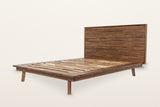 Bassiano bed frame in Warm Pecan acacia, three-quarter view on a warm white studio backdrop: the wide rim, the slats