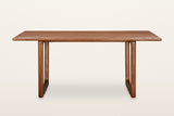 Bernalda dining table in Honey Brown, front view on a warm white studio backdrop: two sled frames set in from the ends