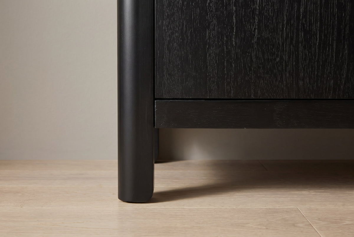 Close-up of a rounded black solid pine corner post becoming a short leg under the bottom rail
