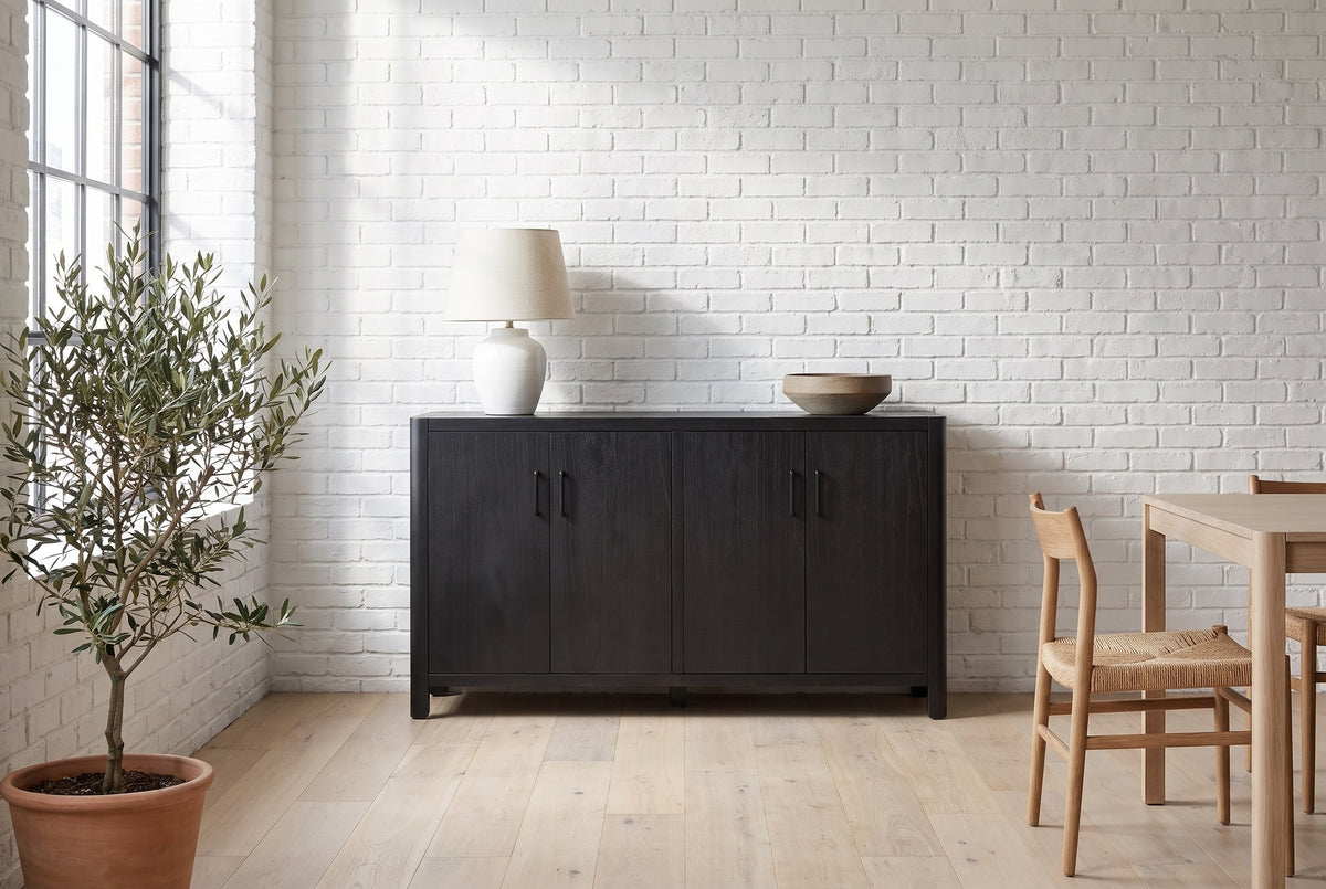 Bibbiena sideboard in black against a white brick wall in a loft dining area, a ceramic lamp and a stoneware bowl on top