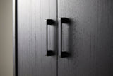 Close-up of two matte black metal bar pulls at the meeting edge of two black-stained wood veneer doors