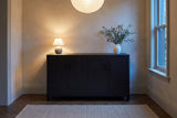 Bibbiena sideboard in a limewashed dining room at dusk, a small lamp lit and olive branches in a white vase