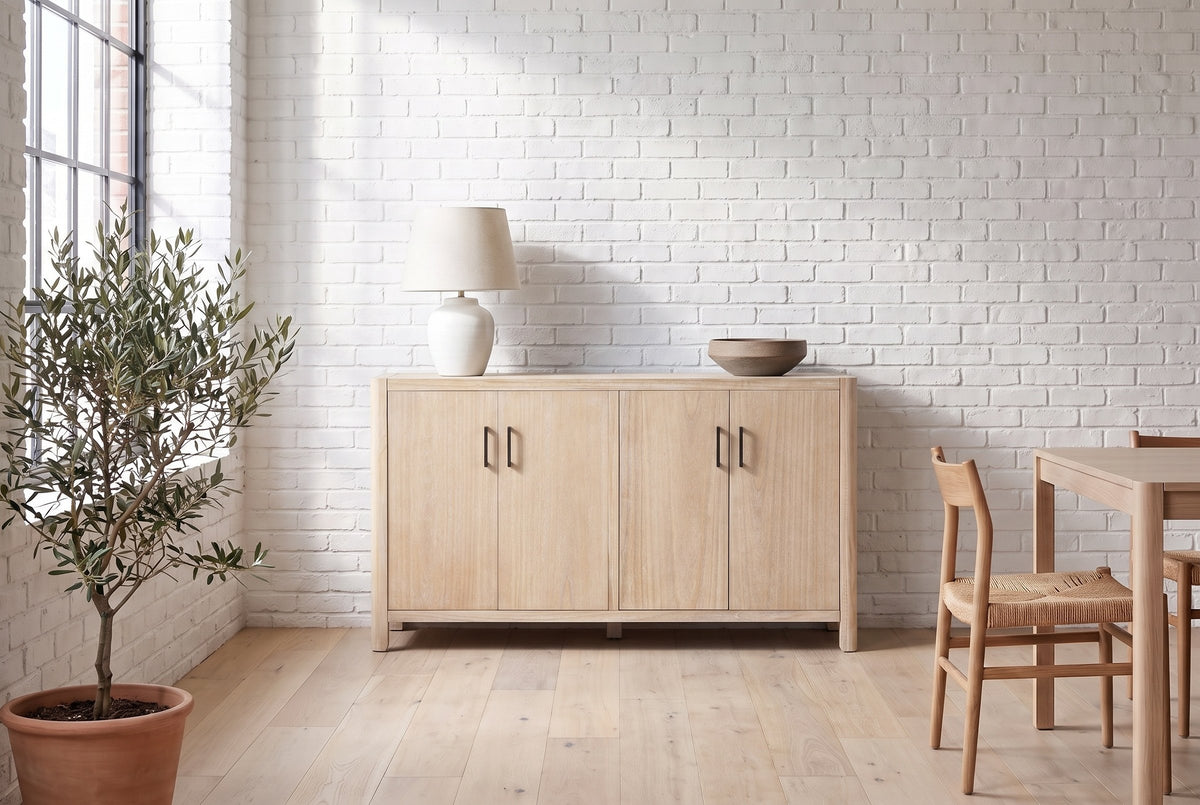 Bibbiena sideboard in Natural against a white brick wall in a loft dining area, a ceramic lamp and a stoneware bowl on top