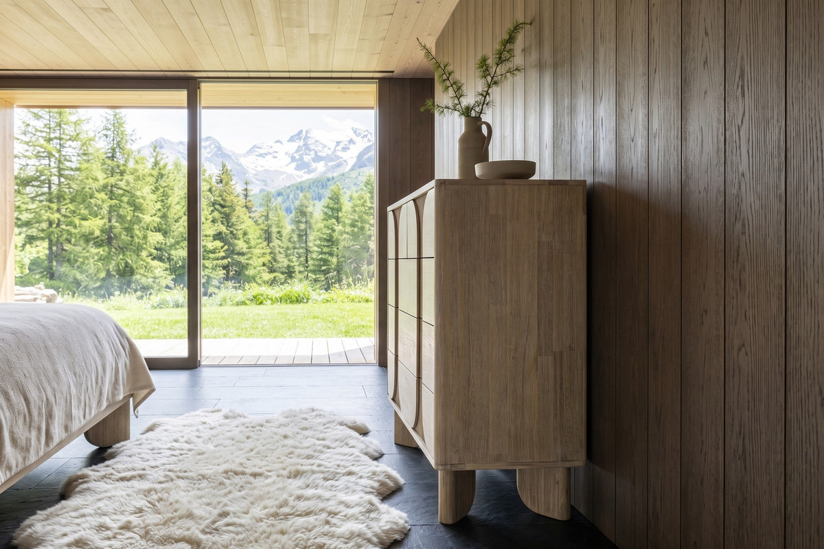 Side view of the Bienno chest in Sand Wash in a Courchevel chalet bedroom, against smoked-oak boards
