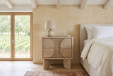 Bienno nightstand in Sand Wash, front view, beside a linen bed in a stone bedroom near Bordeaux, with limestone walls