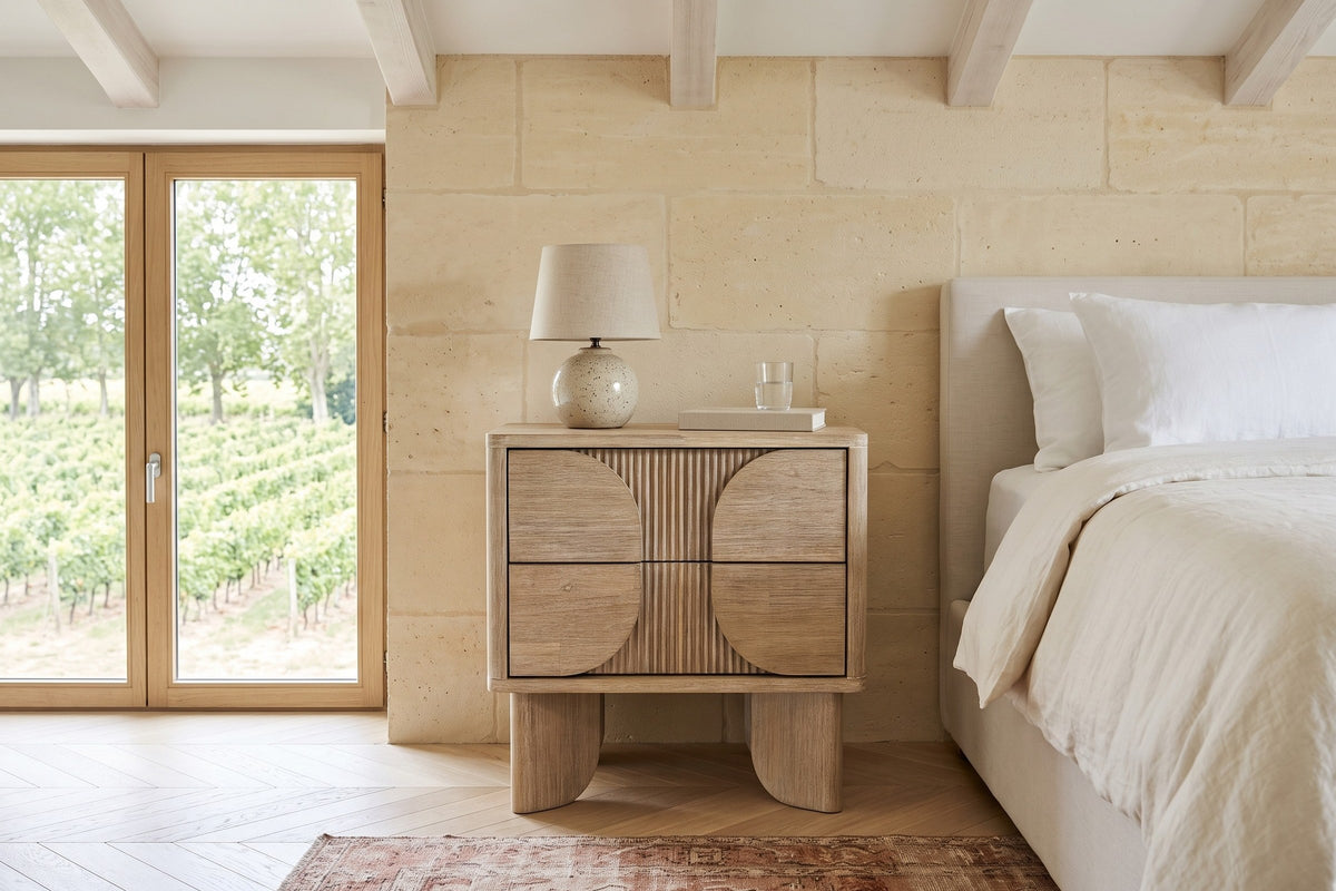 Bienno nightstand in Sand Wash, front view, beside a linen bed in a stone bedroom near Bordeaux, with limestone walls