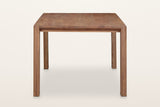 End view of the Bominaco dining table in Brown on a warm white studio backdrop: slim leg ends and a set-back rail under the t