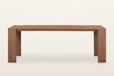 Bominaco dining table in Brown, straight front view on a warm white studio backdrop: the long top flush with two wide slab le