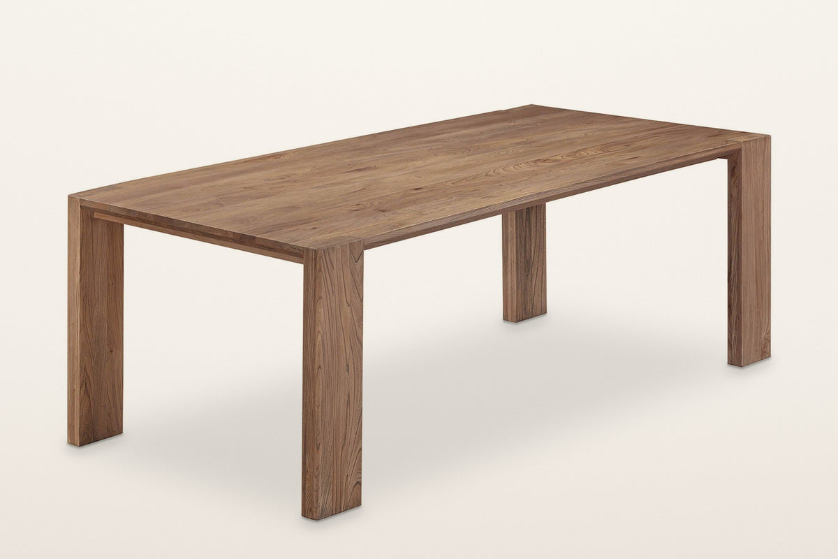 Bominaco wood dining table in Brown, three-quarter view on a warm white studio backdrop: a long top on four flat slab legs