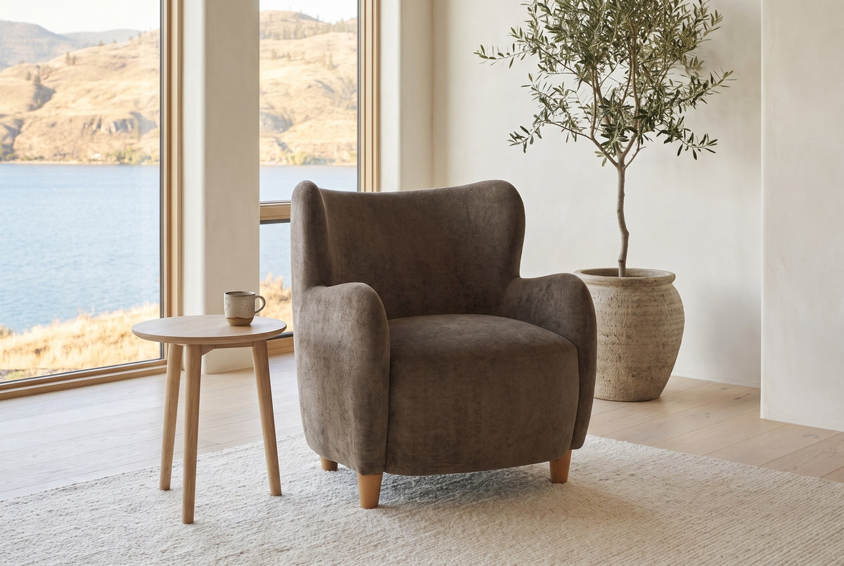 Bormio chair in dark brown velvet beside a pale oak side table in a bright lake-house living room with an olive tree