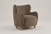 Bormio velvet wingback chair in dark brown, three-quarter view on a warm grey studio backdrop
