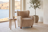 Bormio chair in light camel velvet beside a pale oak side table in a bright lake-house living room with an olive tree