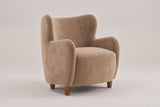 Bormio velvet wingback chair in light camel, three-quarter view on a warm grey studio backdrop