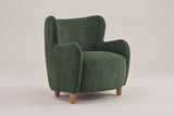 Bormio velvet wingback chair in olive green, three-quarter view on a warm grey studio backdrop