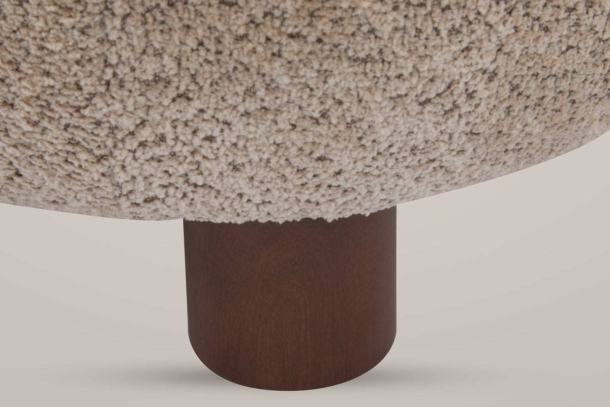 Close-up of a round walnut-finished birch front leg under the curly Light Brown boucle seat