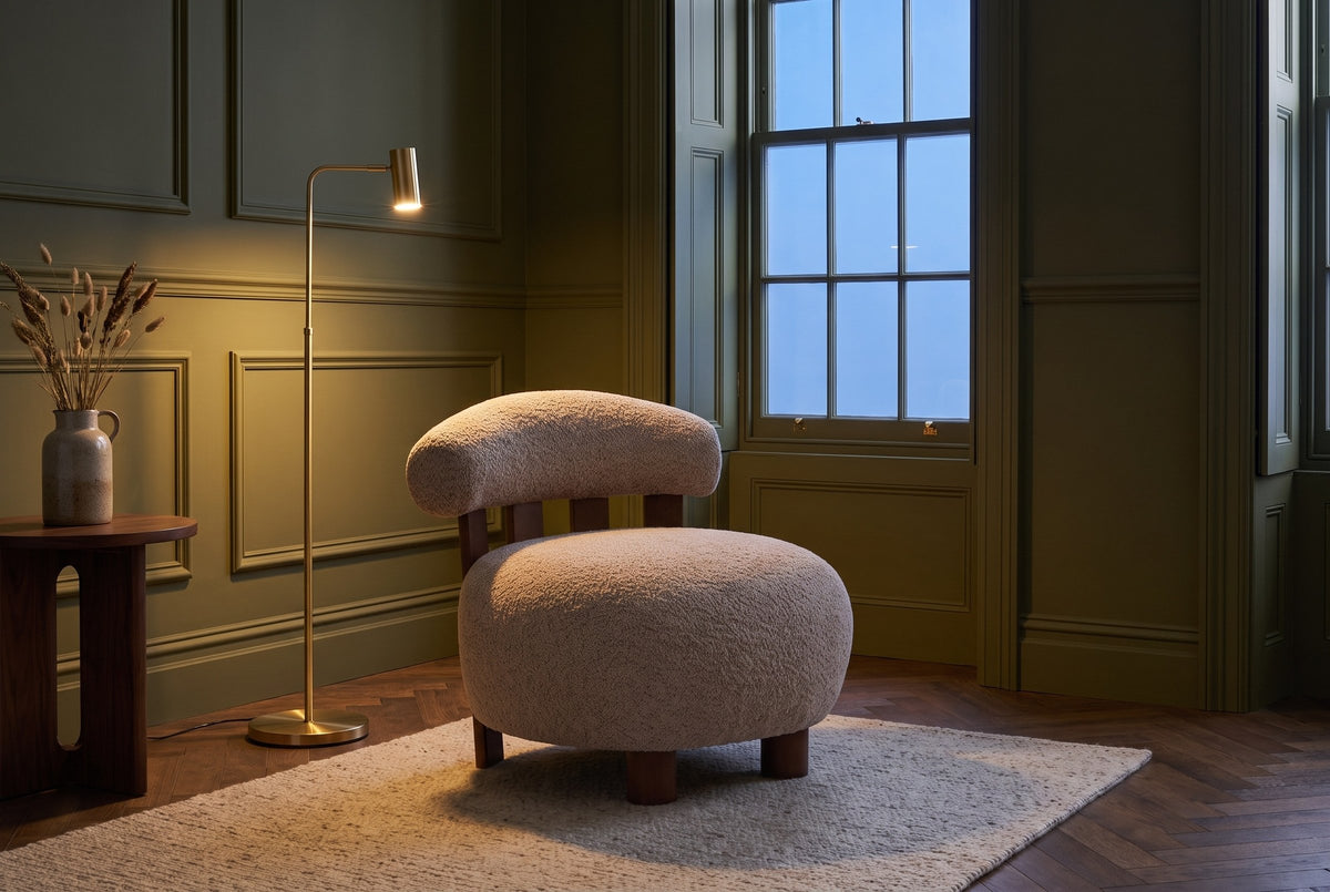 Brescia boucle accent chair in an olive-green panelled sitting room at dusk beside a lit brass floor lamp