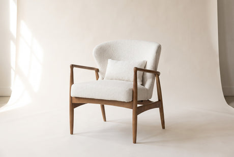 Briar accent chair in Snow, three-quarter view on a warm off-white studio backdrop: soft white fabric on a warm brown ash fra