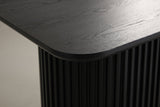 Close-up of the black open-grain top: a softly rounded corner, a slim edge and the fluted pedestal below