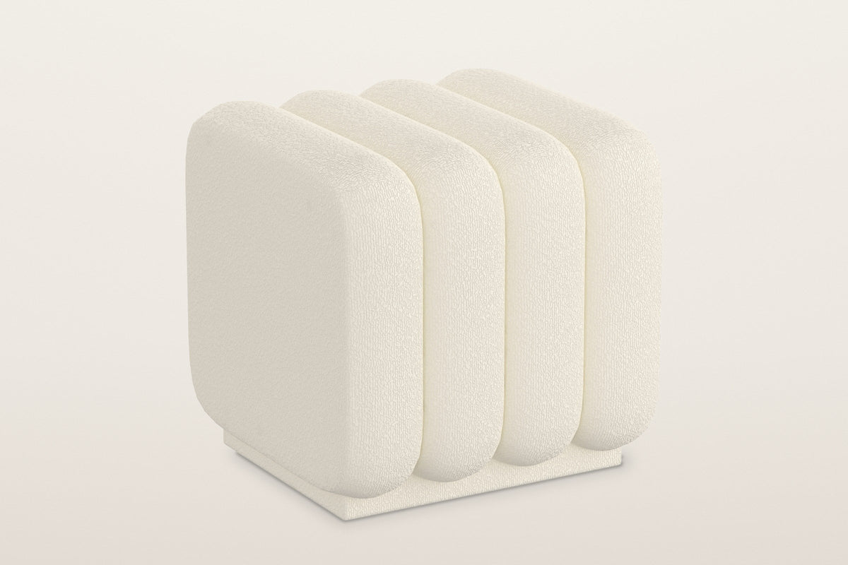 Brusson channel boucle cube ottoman in cream, four rounded channels on a low recessed plinth, three-quarter view on a warm white studio backdrop
