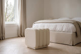 Brusson cube ottoman in cream boucle at the foot of a linen-made bed in a soft white bedroom in Westmount, Montreal, on a herringbone oak floor