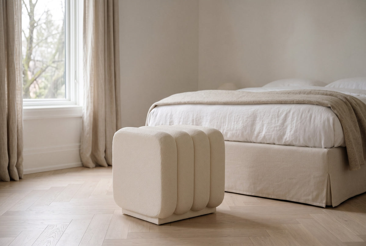 Brusson cube ottoman in cream boucle at the foot of a linen-made bed in a soft white bedroom in Westmount, Montreal, on a herringbone oak floor