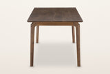 End view of the Calascio dining table in Brown on a warm white studio backdrop: two legs leaning out under the top