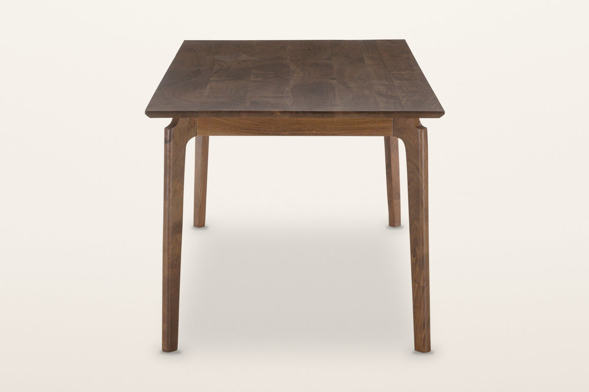 End view of the Calascio dining table in Brown on a warm white studio backdrop: two legs leaning out under the top