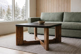 Calcata coffee table in front of a sage-green linen sofa and a cedar-board wall in a Canmore mountain condo, snowy pines through the window