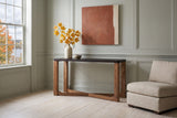 Calcata console table against pale sage panelling in a Fredericton living room, yellow maple leaves in a stoneware jug, an oatmeal linen chair beside it
