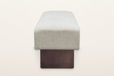 Caltagirone bench in Oatmeal Sand from the end on a warm white studio backdrop: the seat block over the full face of one waln