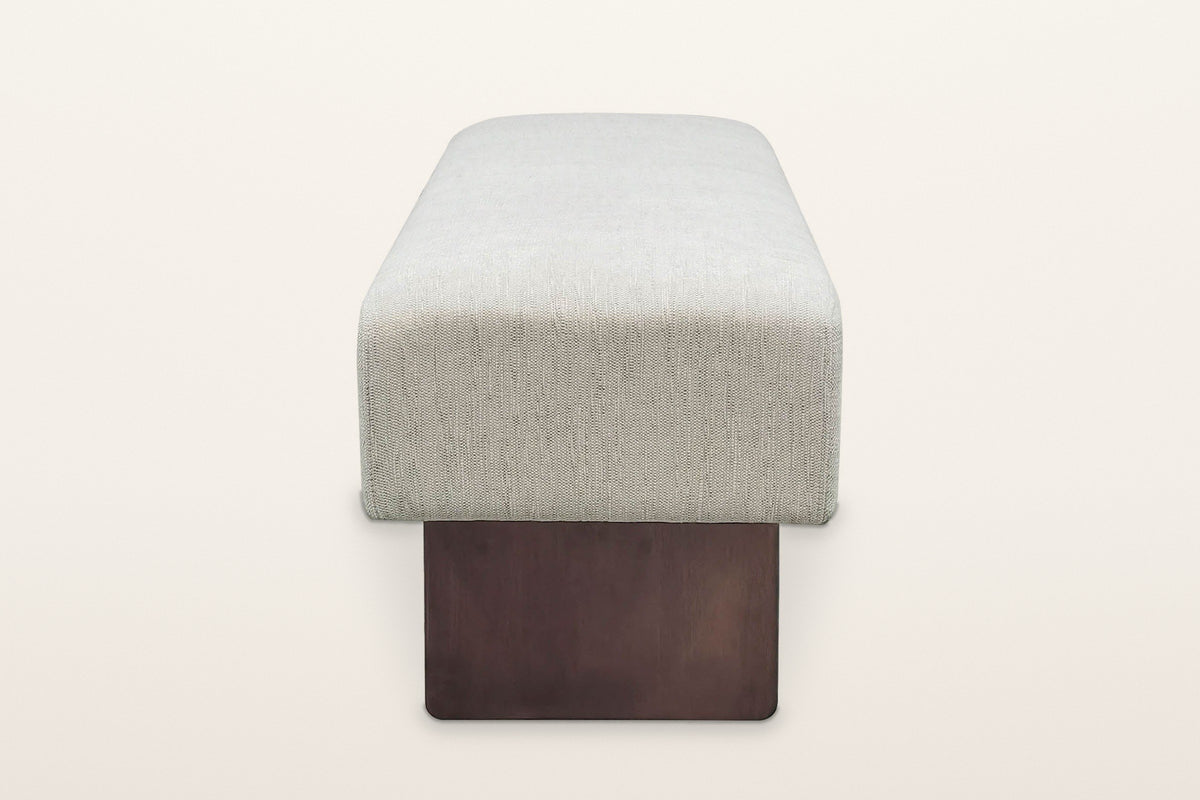 Caltagirone bench in Oatmeal Sand from the end on a warm white studio backdrop: the seat block over the full face of one waln
