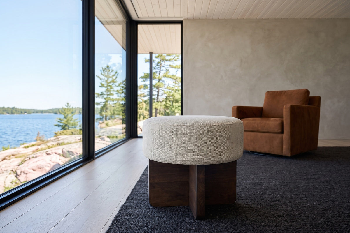 Caltagirone stool in Oatmeal Sand in a Flin Flon lake house, a cognac armchair behind it and a glass wall to granite