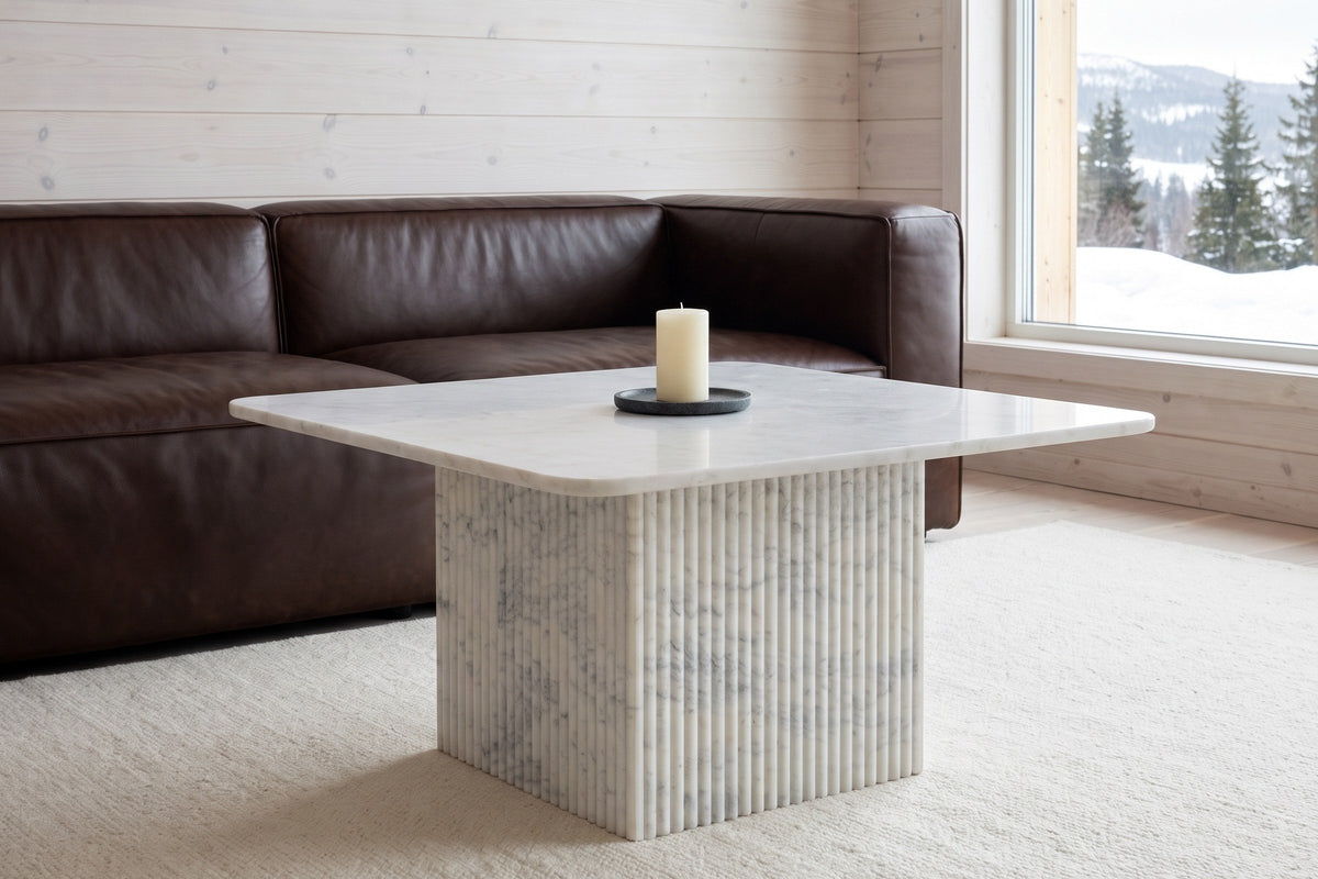 Campiglia white marble coffee table on a cream wool rug in front of a chocolate-brown leather sofa in a Charlevoix chalet