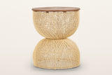 Canale rattan hourglass side table in Natural on a warm white studio backdrop: a round teak top on an open-weave pale rattan