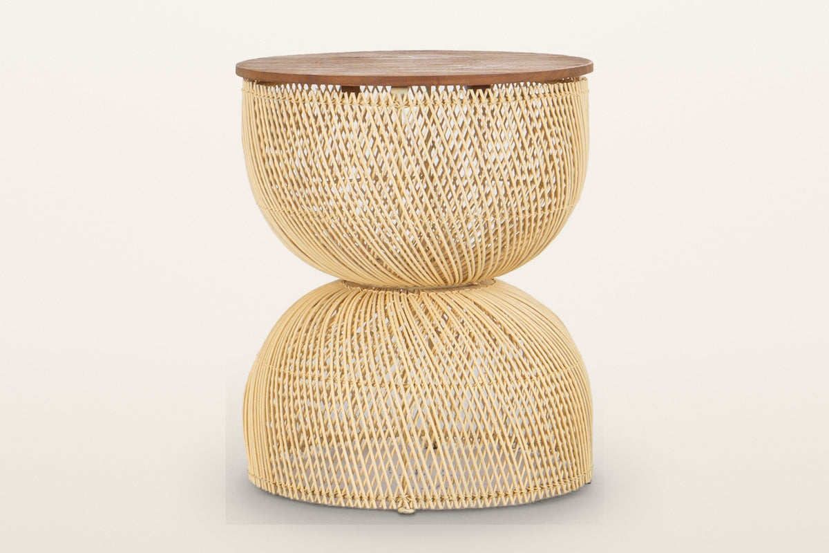 Canale rattan hourglass side table in Natural on a warm white studio backdrop: a round teak top on an open-weave pale rattan