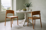 Two Canelli dining chairs in natural oak at a round white pedestal table in a Victoria dining room with sage-green walls