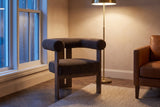 Caorle chair in an Ottawa townhouse reading corner at dusk, a brass floor lamp lit beside a cognac leather sofa