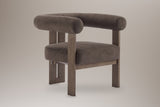 Caorle velvet round-arm accent chair in dark brown, three-quarter view on a warm grey studio backdrop