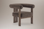Caorle velvet round-arm accent chair in dark brown, three-quarter view on a warm grey studio backdrop